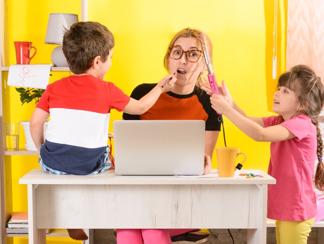 Woman working from home with kids while they curl her hair and apply makeup to show how crazy things are