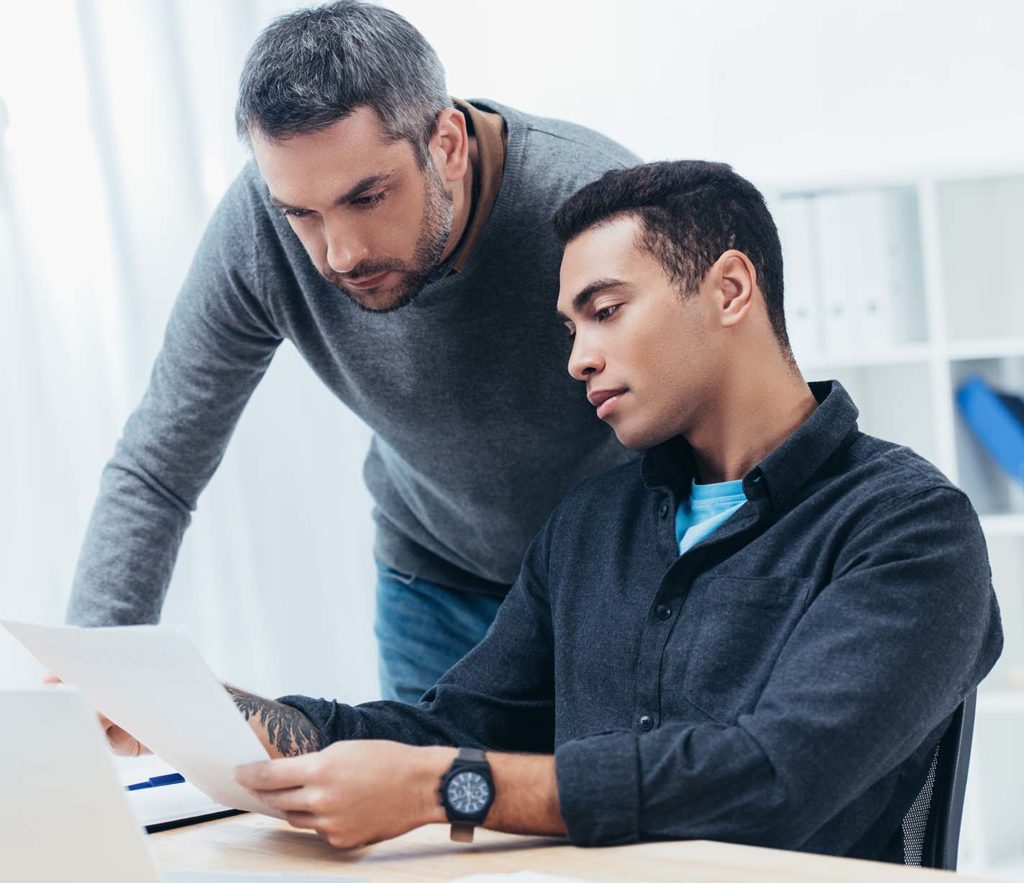 bearded-mentor-looking-at-young-colleague-working